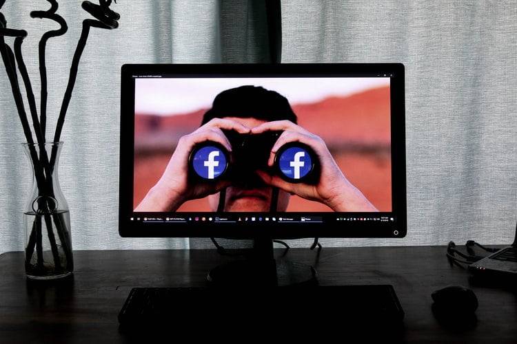 Een beeldscherm met daarop een man die door een verrekijker kijkt waarvan beide lenzen het Facebook-logo zijn
