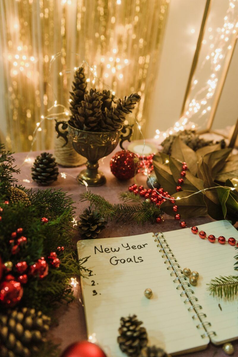 Een opengeslagen notitieboek met de handgeschreven kop New Year Goals en drie lege regels, tussen kerstversiering en lichtjes