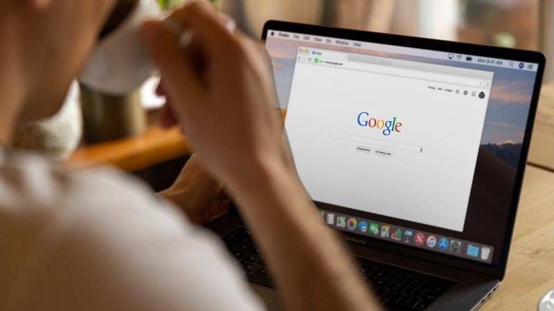 Iemand kijkt met een kop koffie in de hand naar een laptop met de startpagina van Google
