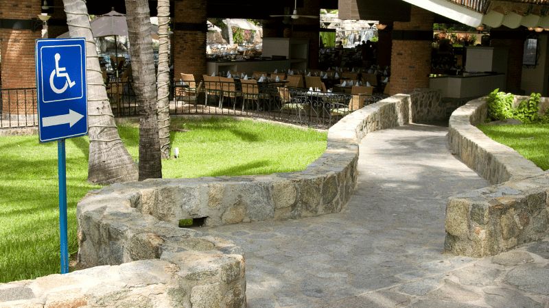 Een gemetseld pad zonder drempels naar een restaurantterras, met een bord dat de rolstoeltoegang aanwijst