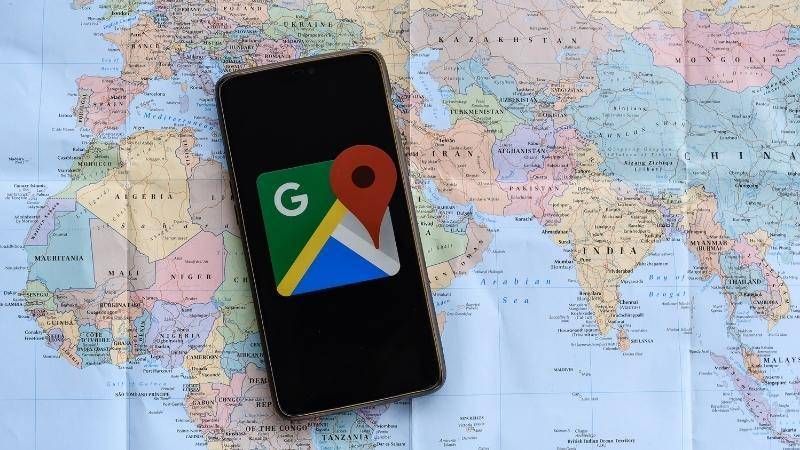 Een telefoon met het logo van Google Maps op het scherm, liggend op een papieren wereldkaart