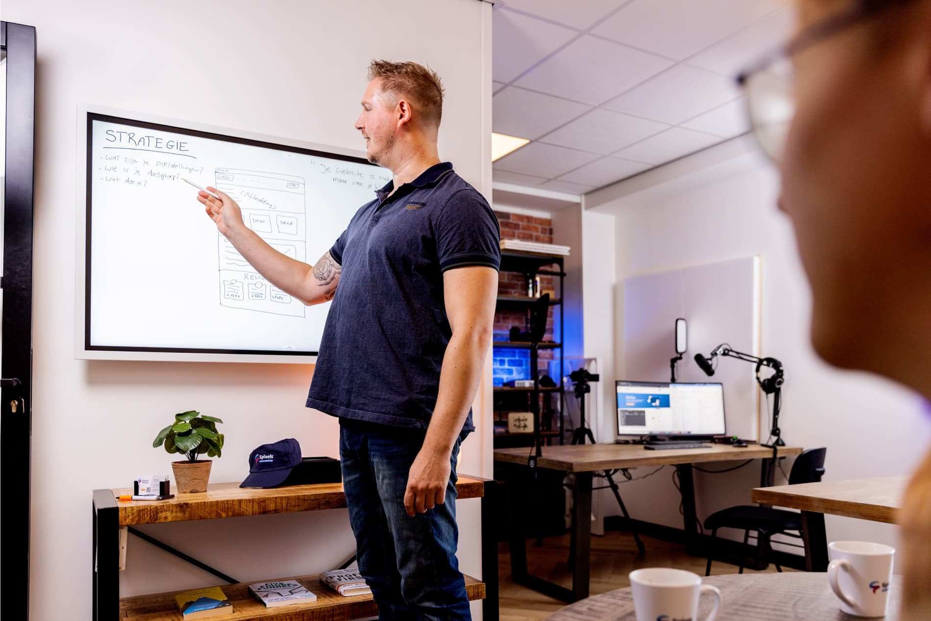Sven Kersten wijst tijdens een sessie naar een whiteboard met het woord Strategie, de vragen over doelstellingen en doelgroep, en een geschetste paginaopbouw