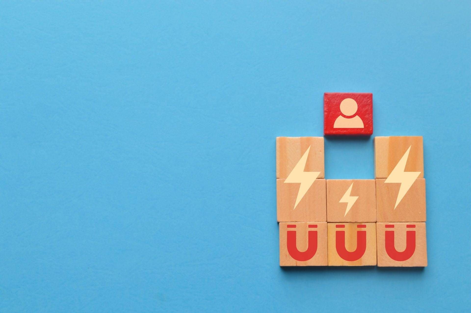 Houten blokjes met magneet- en bliksemsymbolen trekken een rood blokje met een poppetje erop naar zich toe